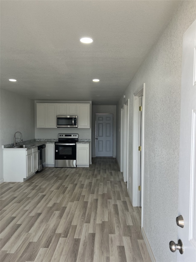 Kitchen featuring white cabinetry, stainless steel appliances, light wood-style flooring, a textured wall, and recessed lighting