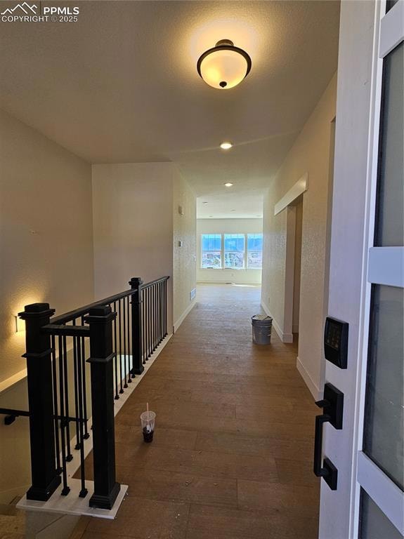 Hall with wood finished floors, an upstairs landing, a textured wall, and a textured ceiling