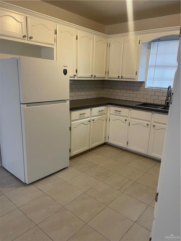 Kitchen with white fridge, dark countertops, white cabinetry, and backsplash