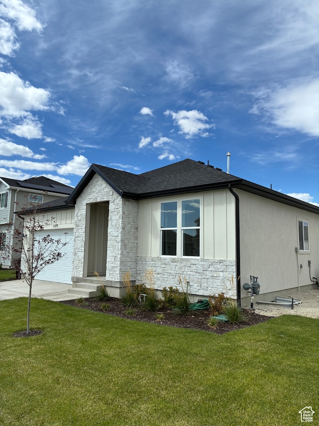 View of front facade with stone siding, a front lawn, roof with shingles, and driveway