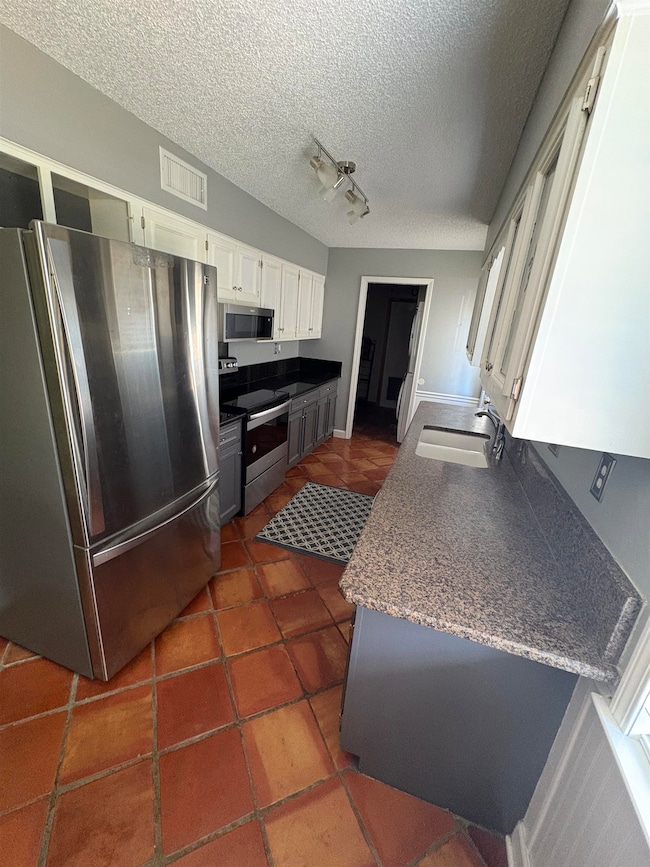Kitchen featuring stainless steel appliances, white cabinetry, a textured ceiling, dark tile patterned floors, and rail lighting