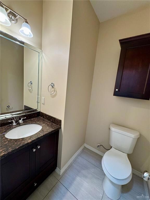 Half bathroom featuring tile patterned floors, vanity, toilet, and baseboards