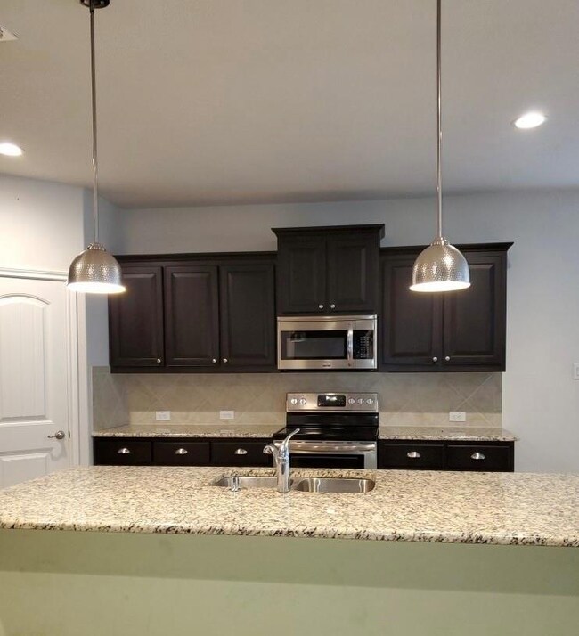 Kitchen featuring tasteful backsplash, light stone counters, hanging light fixtures, appliances with stainless steel finishes, and sink
