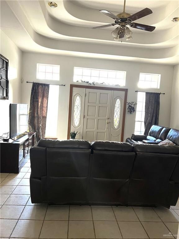 Tiled living room with a healthy amount of sunlight, ceiling fan, and a tray ceiling