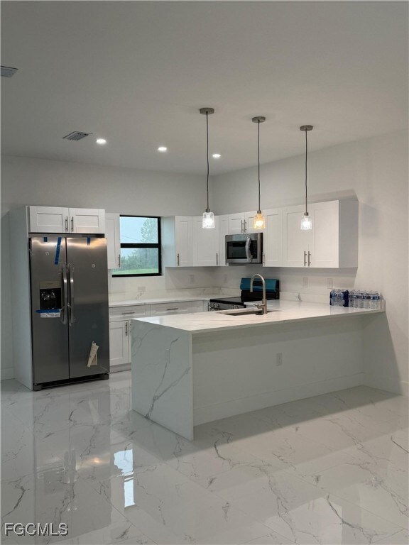 Kitchen featuring white cabinets, light marble finish flooring, stainless steel appliances, a peninsula, and recessed lighting