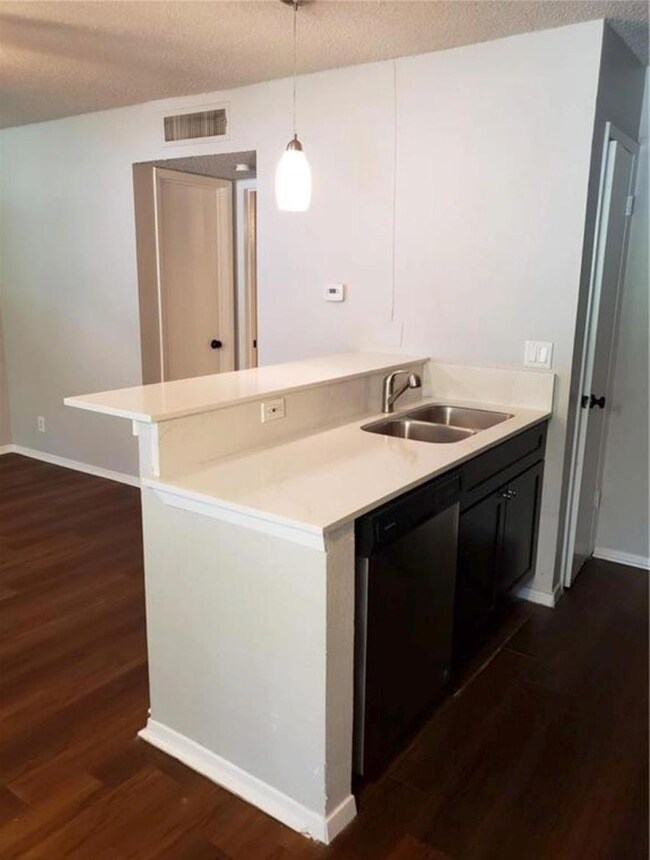 Kitchen featuring a textured ceiling, light countertops, dark wood-style flooring, dishwashing machine, and pendant lighting