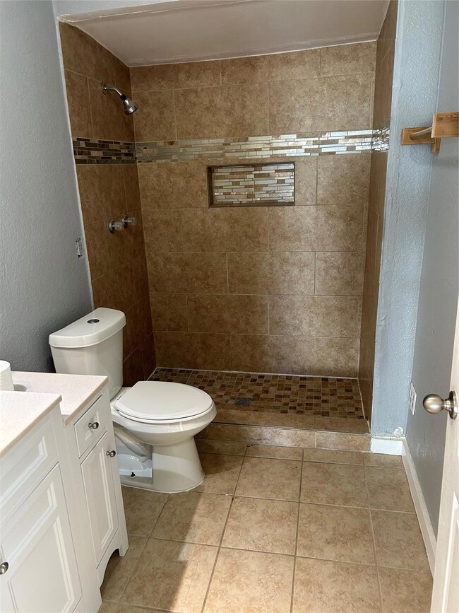 Bathroom with toilet, vanity, tiled shower, and tile patterned floors
