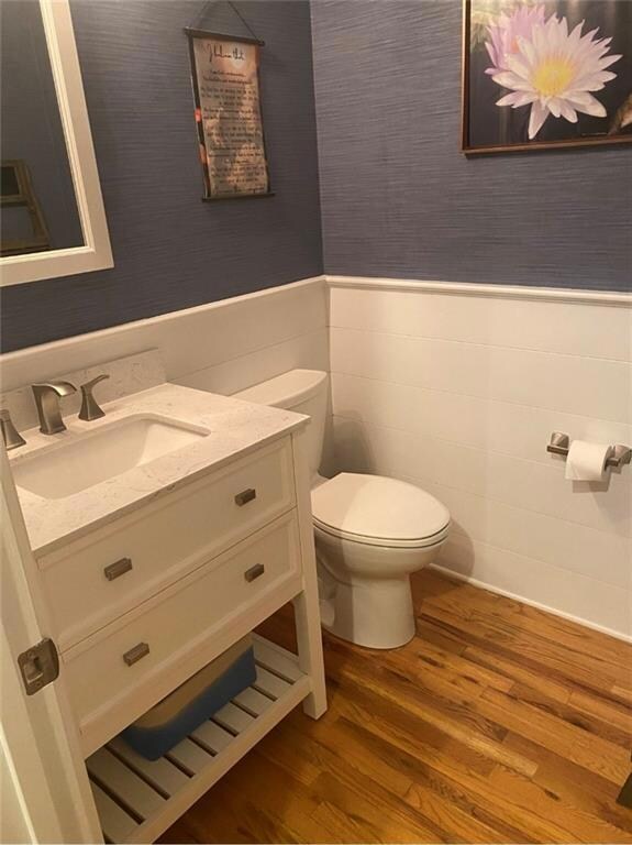 Bathroom featuring wood finished floors, vanity, a wainscoted wall, and wallpapered walls