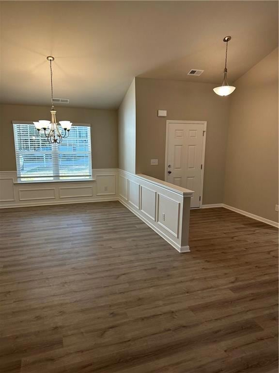 Unfurnished dining area featuring dark wood-style floors, a chandelier, and a decorative wall