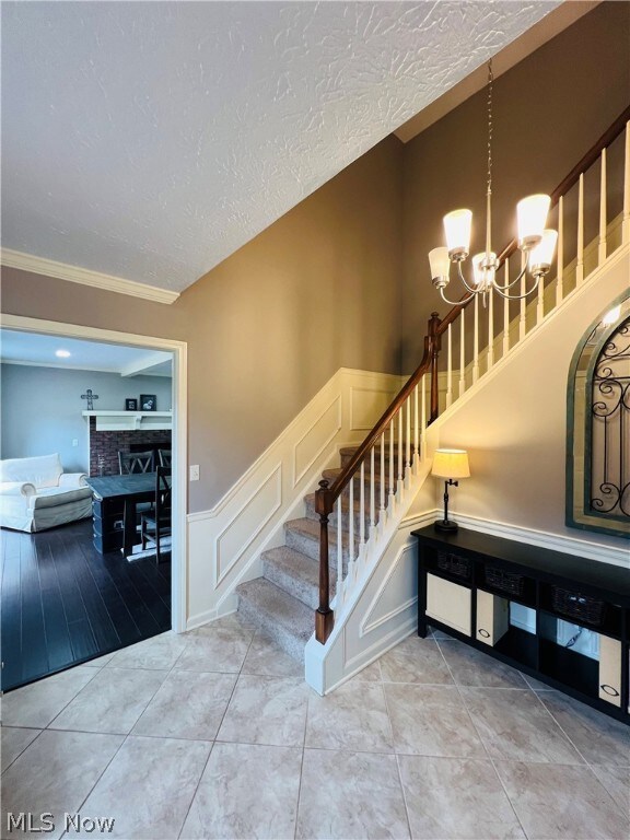Stairs featuring wood-type flooring, a textured ceiling, a chandelier, and ornamental molding