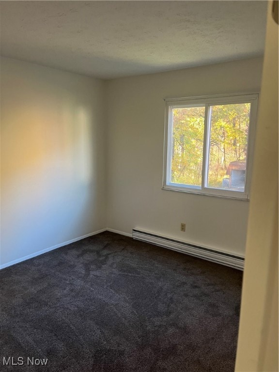 Empty room with a baseboard heating unit and dark colored carpet
