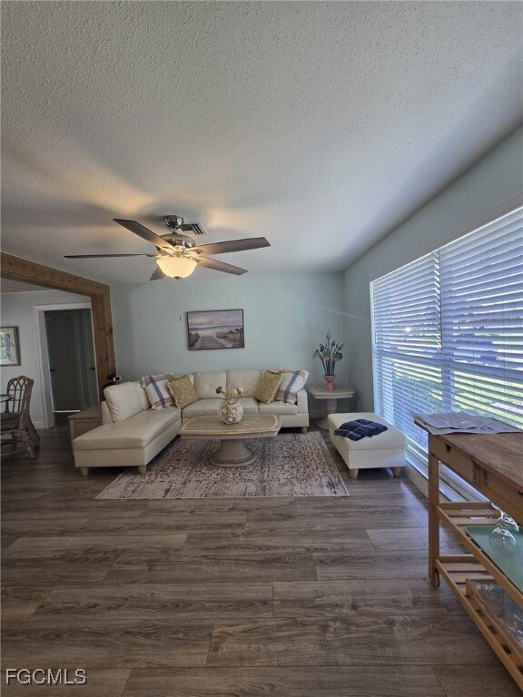 Living area featuring dark wood-style floors, ceiling fan, and a textured ceiling
