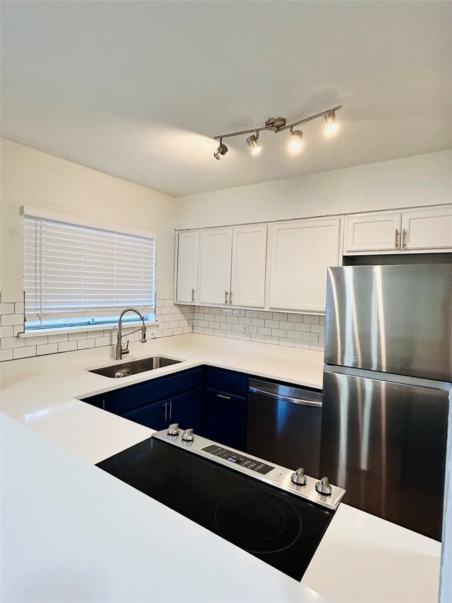 Kitchen with white cabinets, stainless steel appliances, backsplash, and blue cabinetry