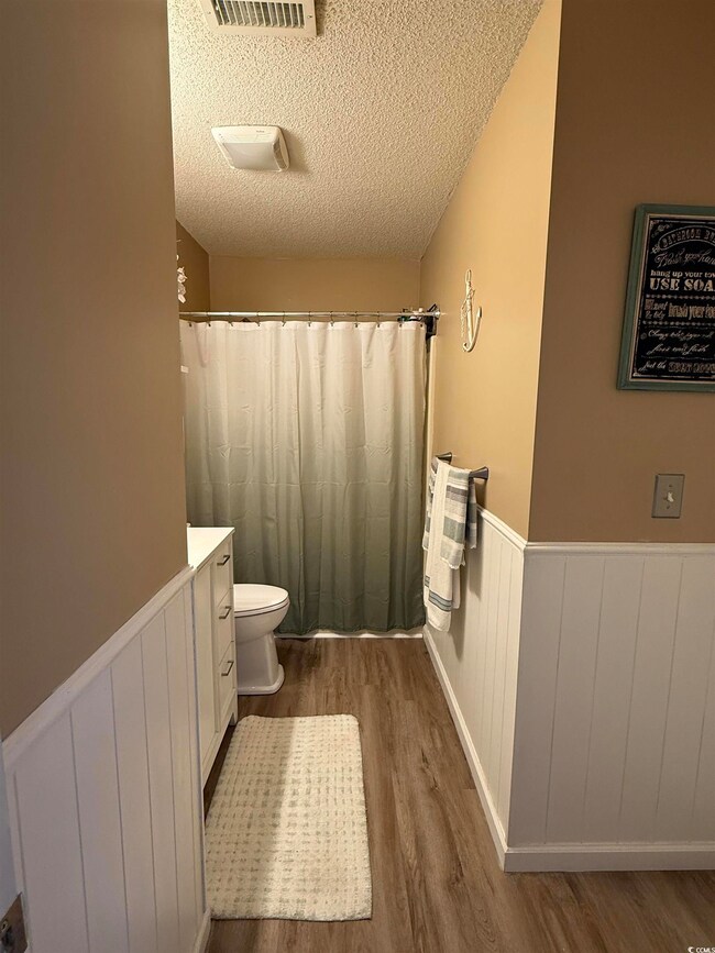 Full bath with a textured ceiling, a wainscoted wall, curtained shower, dark wood-style floors, and vanity