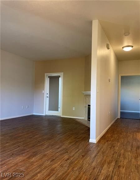 Unfurnished room with dark wood-style floors and a tiled fireplace
