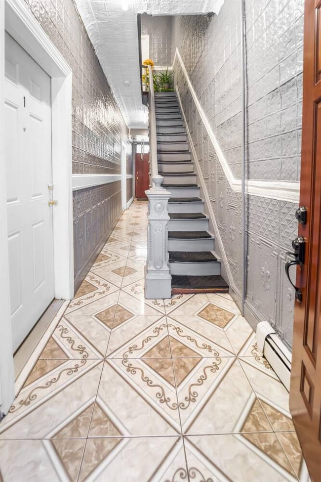 Entrance foyer with a baseboard radiator, light tile patterned floors, and stairs