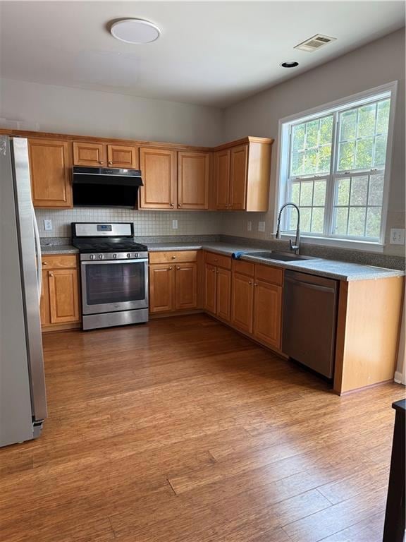 Kitchen with stove, fridge, dishwashing machine, light wood finished floors, and decorative backsplash
