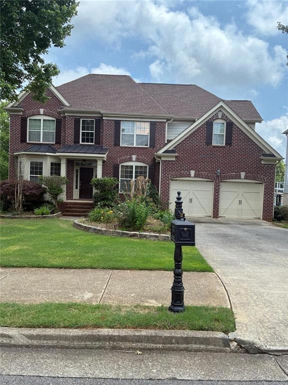 View of front of home with concrete driveway, brick siding, a front yard, and roof with shingles