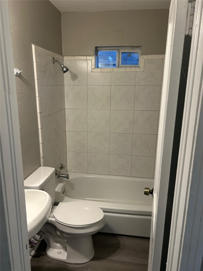 Bathroom with shower / bathtub combination, wood finished floors, and a textured wall
