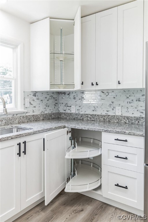 Kitchen with backsplash, hardwood flooring, white cabinetry, and granite countertops