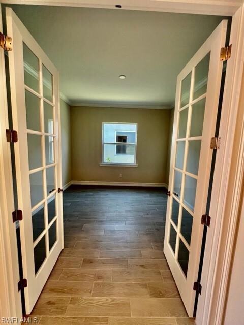 Unfurnished room featuring french doors, crown molding, wood finished floors, and baseboards