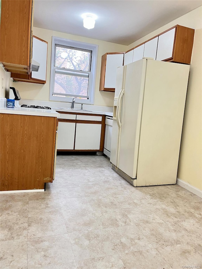 Kitchen featuring brown cabinetry, white appliances, light countertops, and white cabinetry