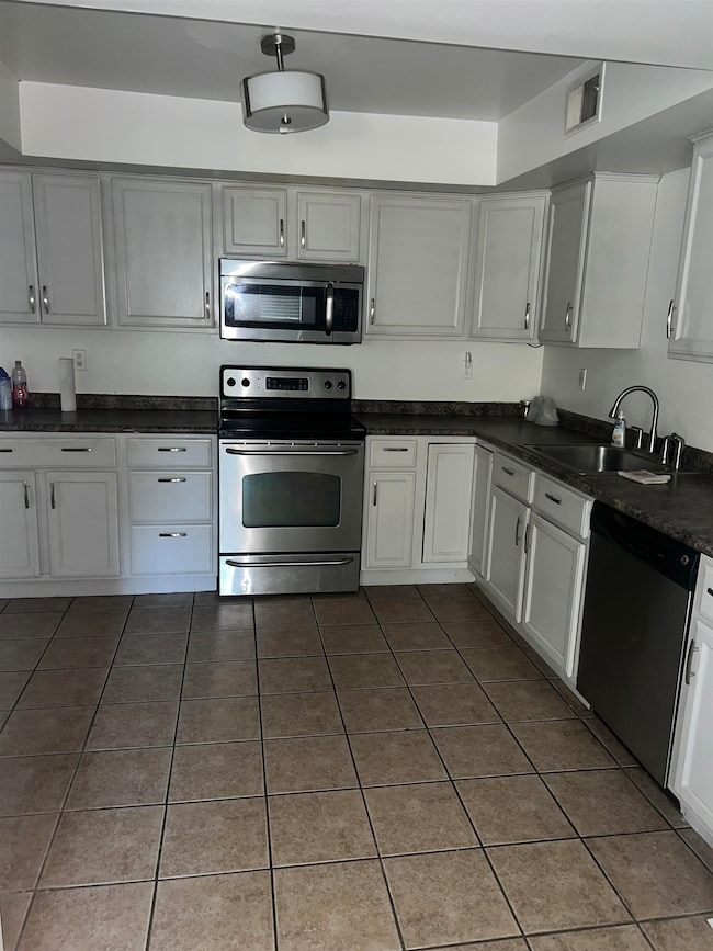 Kitchen featuring appliances with stainless steel finishes, dark tile patterned flooring, dark countertops, and white cabinetry