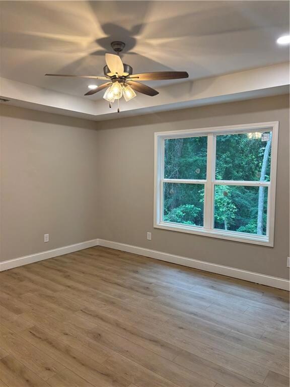 Spare room with a ceiling fan, wood finished floors, and a raised ceiling