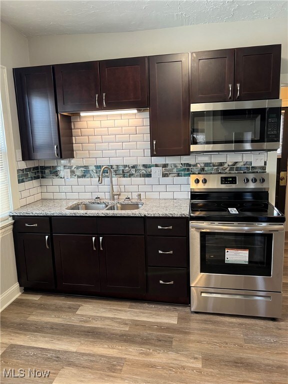Kitchen with light wood finished floors, light stone countertops, decorative backsplash, stainless steel appliances, and a sink