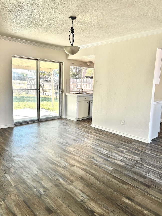 Unfurnished dining area featuring ornamental molding, dark wood-type flooring, and a textured ceiling