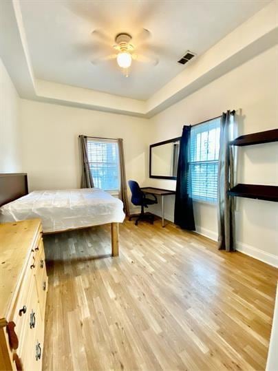 Bedroom with a raised ceiling, light wood-style flooring, a ceiling fan, and an office area