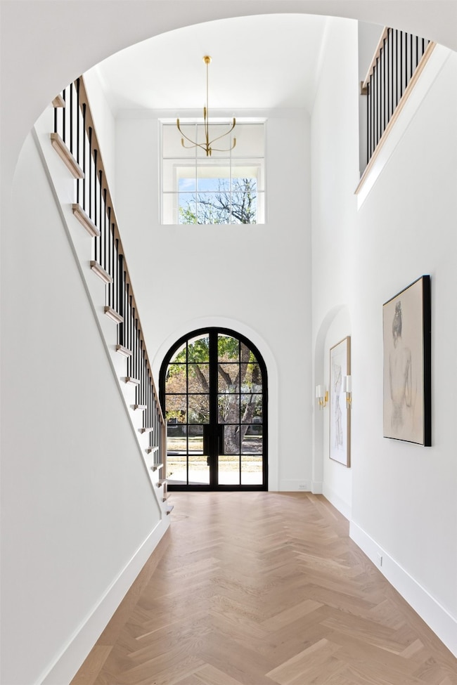 Foyer featuring arched walkways, french doors, stairs, a towering ceiling, and a chandelier