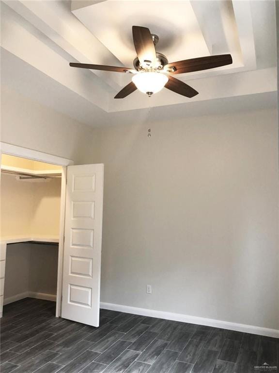 Unfurnished bedroom with a tray ceiling, ceiling fan, wood finish floors, and a walk in closet
