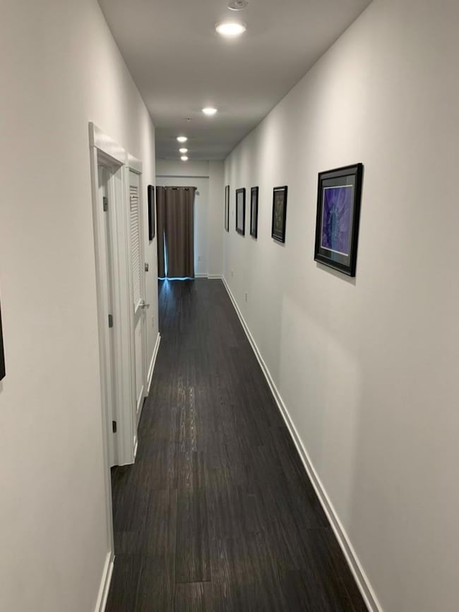 Corridor featuring baseboards, dark wood-style fl