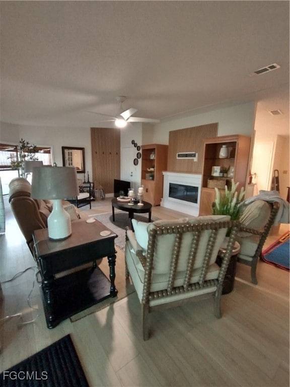 Living area featuring a glass covered fireplace, light wood finished floors, and a ceiling fan
