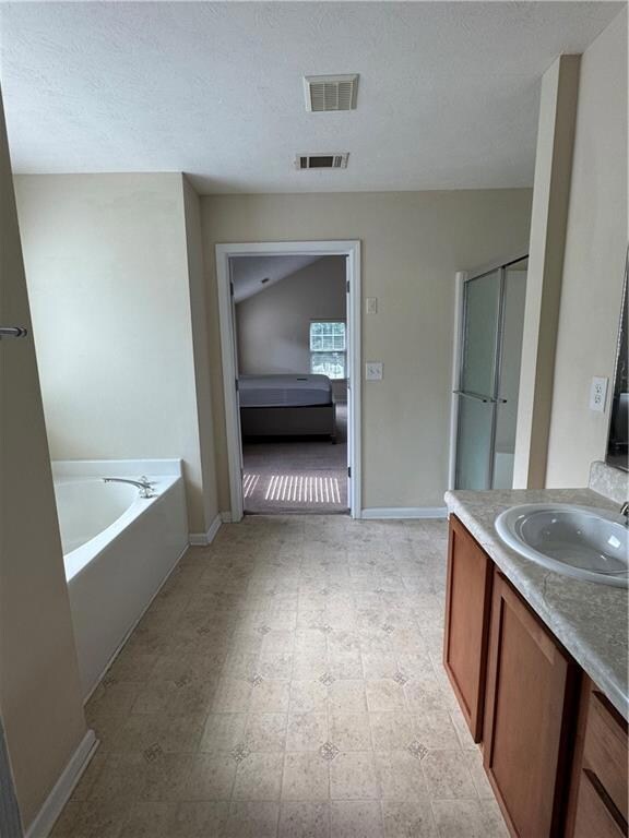 Ensuite bathroom featuring vanity, a shower stall, a bath, a textured ceiling, and light flooring