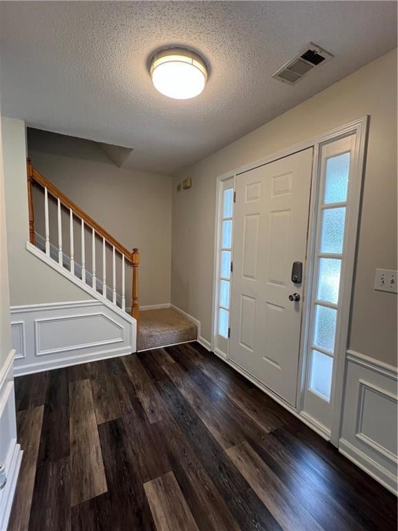 Foyer entrance with stairs, dark wood-type flooring, a textured ceiling, a wainscoted wall, and a decorative wall
