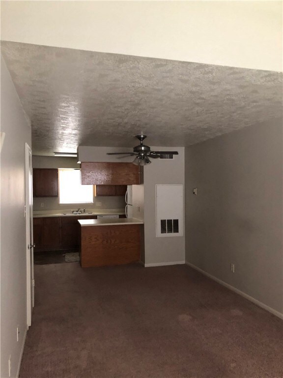 Kitchen featuring ceiling fan, sink, dark carpet, and a textured ceiling