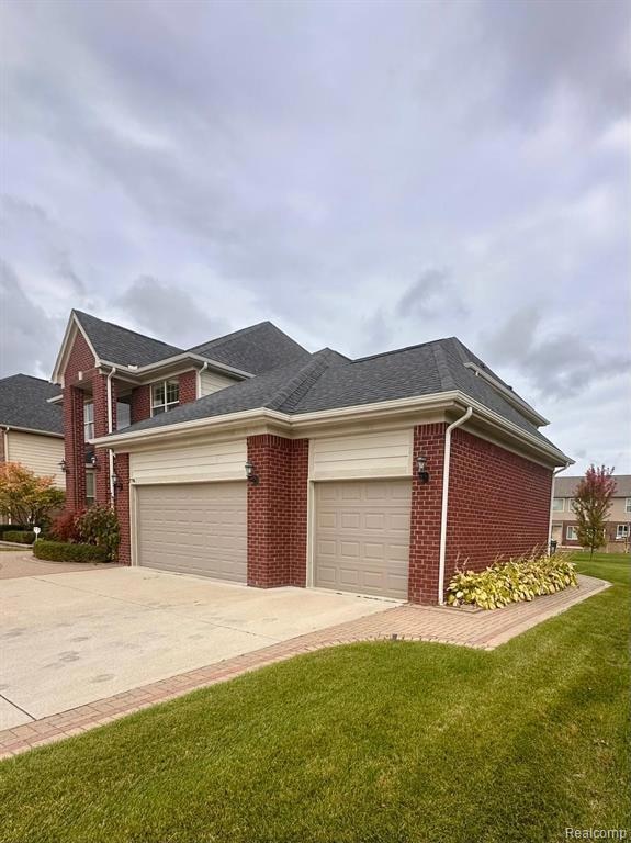View of front facade featuring a shingled roof, driveway, brick siding, and a front yard