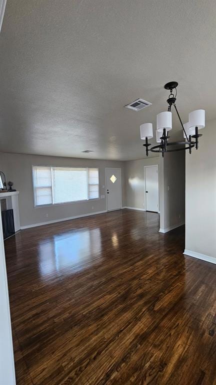 Unfurnished living room with a textured ceiling, a chandelier, and dark wood-style floors