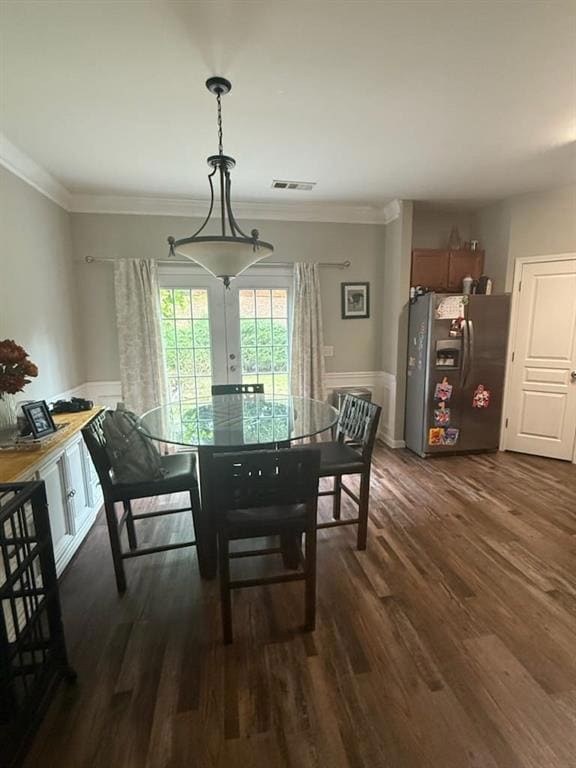 Dining space featuring dark wood-type flooring, a wainscoted wall, and crown molding