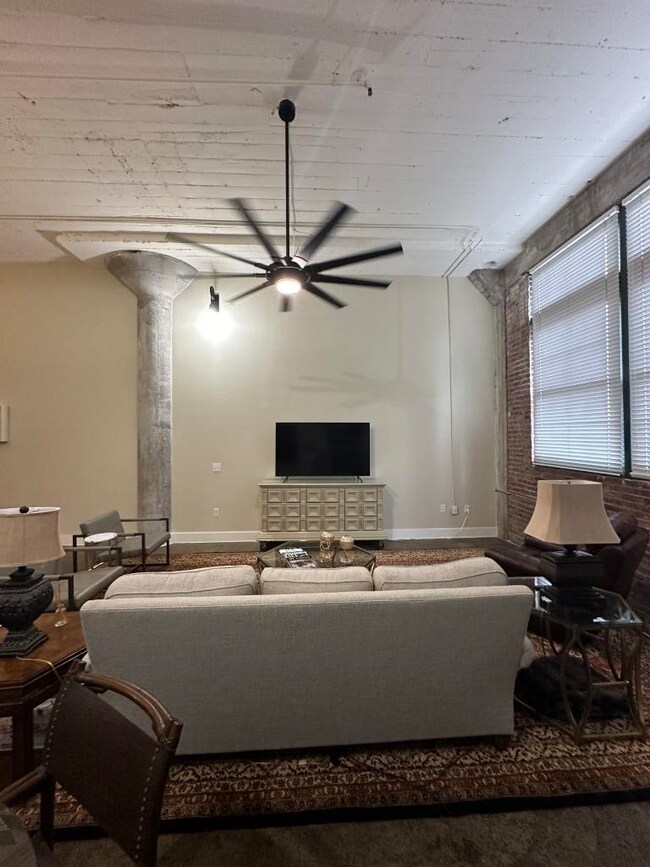 Carpeted living room featuring ceiling fan and decorative columns