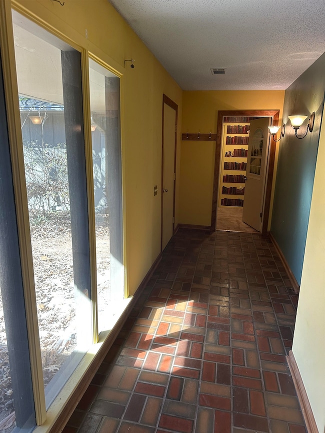 Hall with a textured ceiling, brick floor, visible