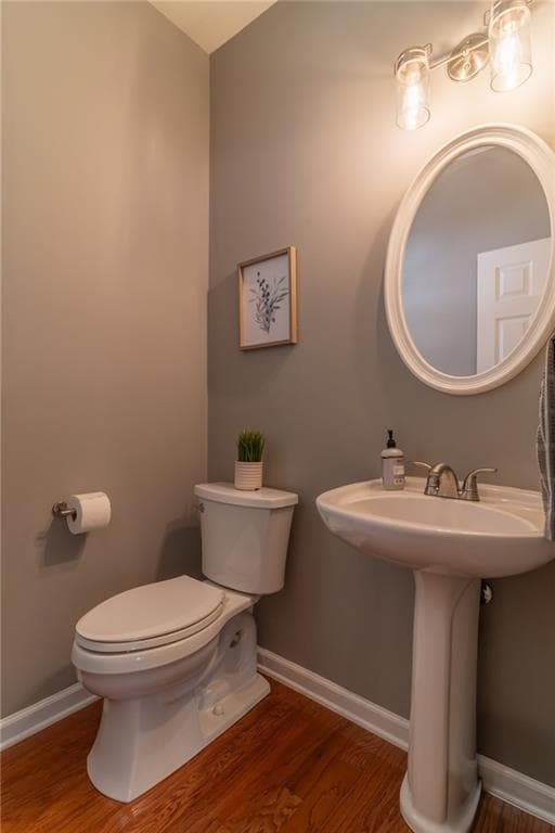 Half bath featuring toilet, wood finished floors, baseboards, and a sink