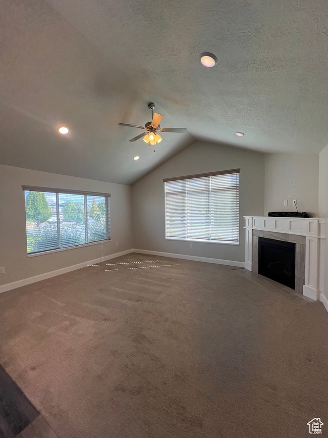 Unfurnished living room with a tiled fireplace, lofted ceiling, carpet flooring, a ceiling fan, and a textured ceiling