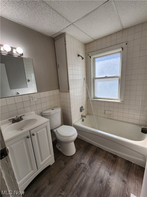Full bathroom with tile walls, tiled shower / bath combo, hardwood floors, and a paneled ceiling