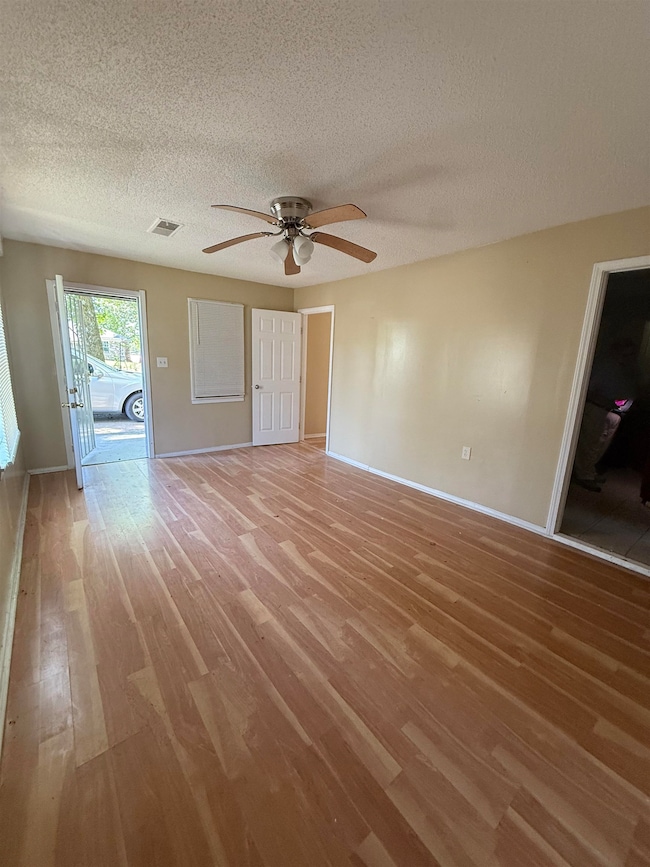 Unfurnished living room featuring light wood-style flooring, ceiling fan, a textured ceiling, and baseboards