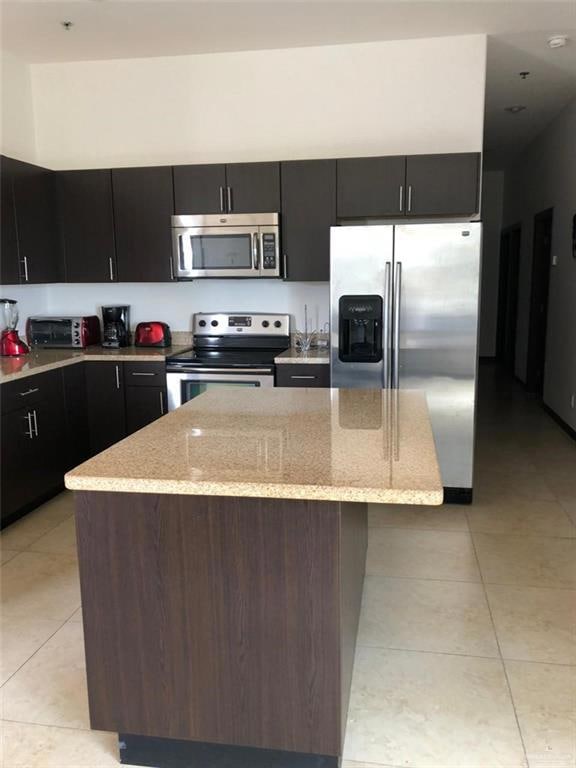 Kitchen featuring appliances with stainless steel finishes, light tile patterned floors, light stone counters, and a center island