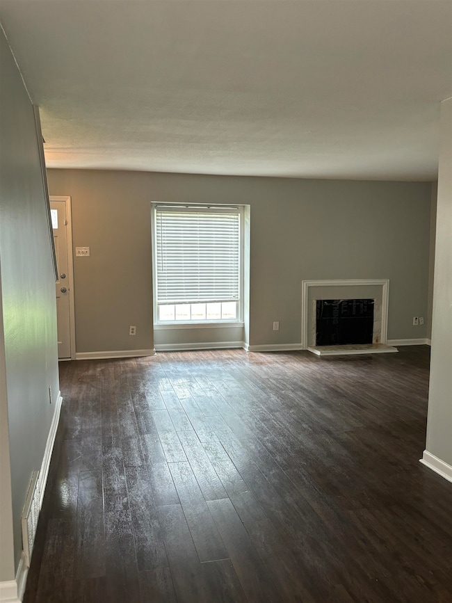 Unfurnished living room with dark wood finished floors, a glass covered fireplace, and baseboards