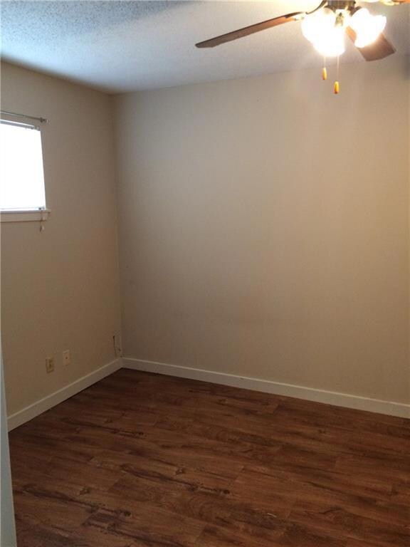 Empty room with ceiling fan, dark wood-style floors, and a textured ceiling